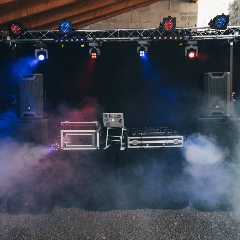 DJ-Setup mit Lautsprechern, Mischpult und Lichteffekten in nebliger Atmosphäre.