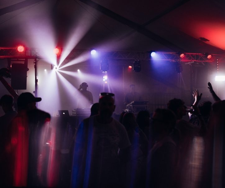 Dunkle Tanzfläche mit bunten Lichtern und feiernden Menschen.