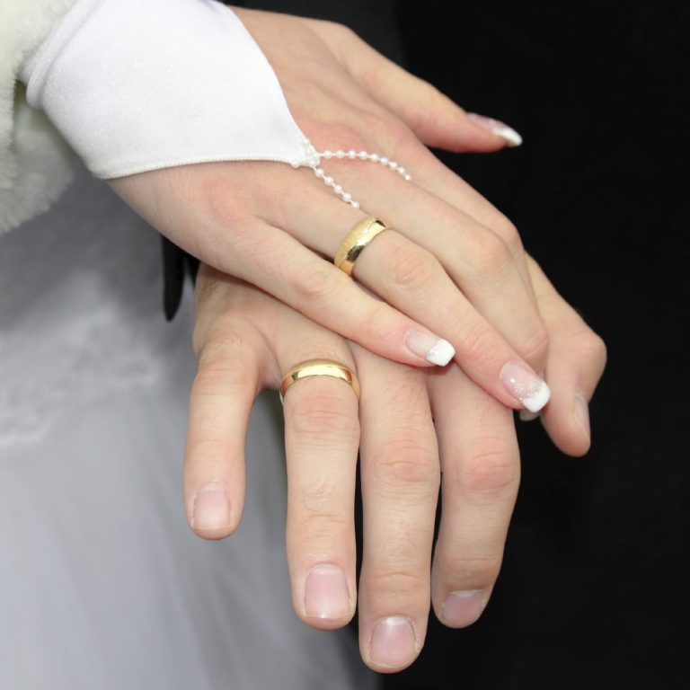 Hochzeitsringe auf den zusammengehaltenen Händen eines Paares.