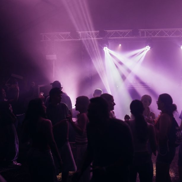 Menschen tanzen auf einer beleuchteten Tanzfläche mit Nebel und bunten Lichtern.