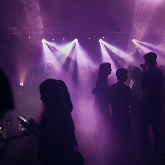 Dunkle Silhouetten von Personen in einer von Lichtern erleuchteten Umgebung mit Nebel.