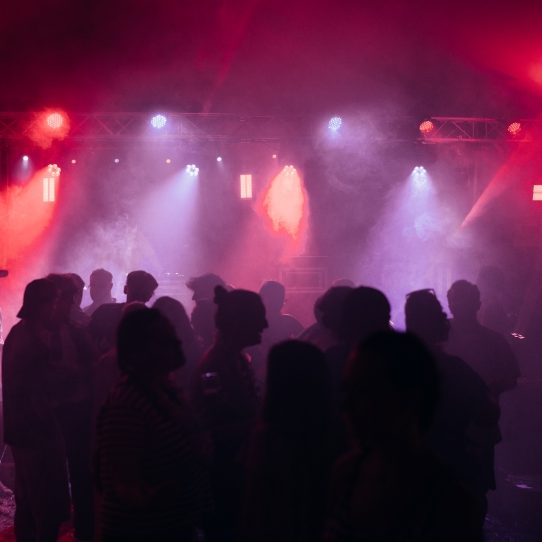 Silhouetten von Menschen bei einer Clubveranstaltung mit bunten Lichtern und Nebel.