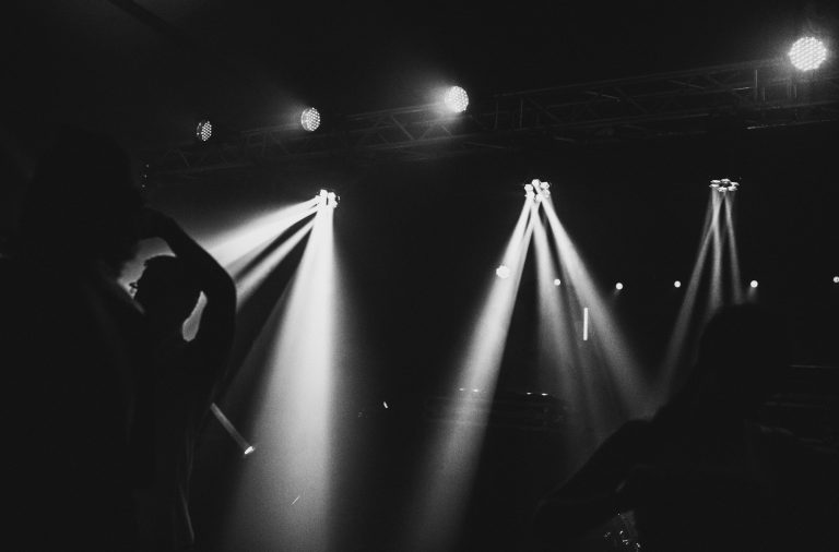 Veranstaltungstechnik Silhouetten von Menschen vor Bühnenlichtern in Schwarz-Weiß.