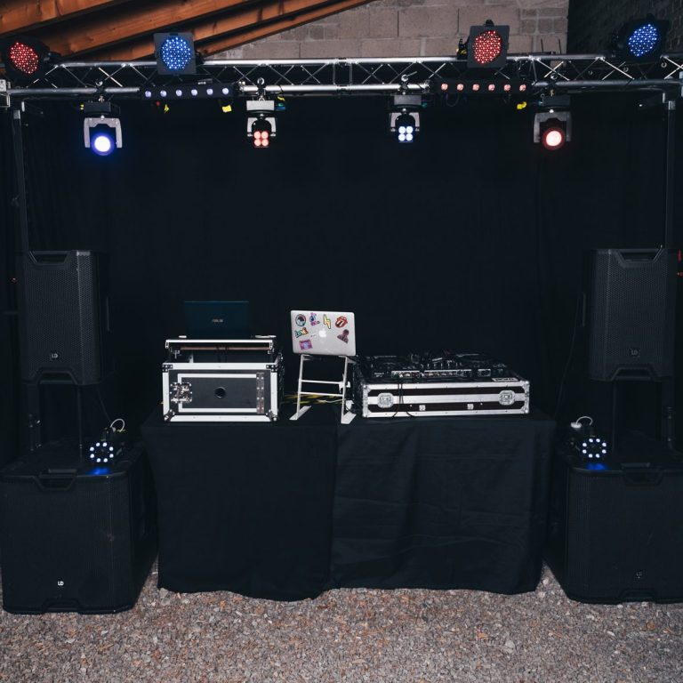 DJ-Pult mit Lautsprechern und Scheinwerfern, vor schwarzem Hintergrund aufgebaut.